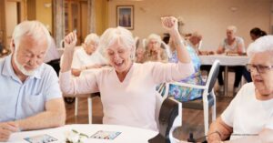 Seniors smiling and playing bingo together in a senior living community activity room.