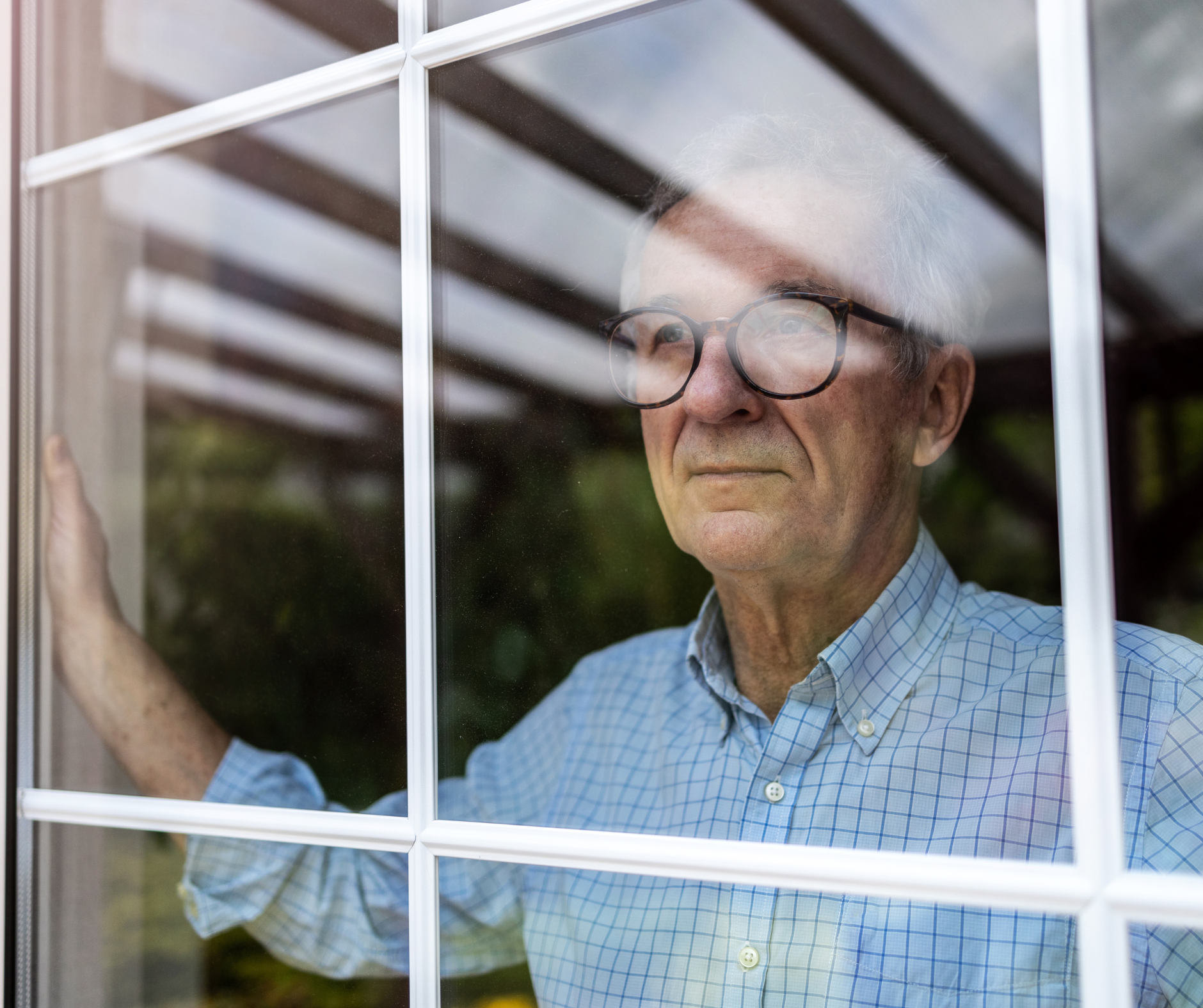 older adult man looking out window appearing lonely and reflective at home