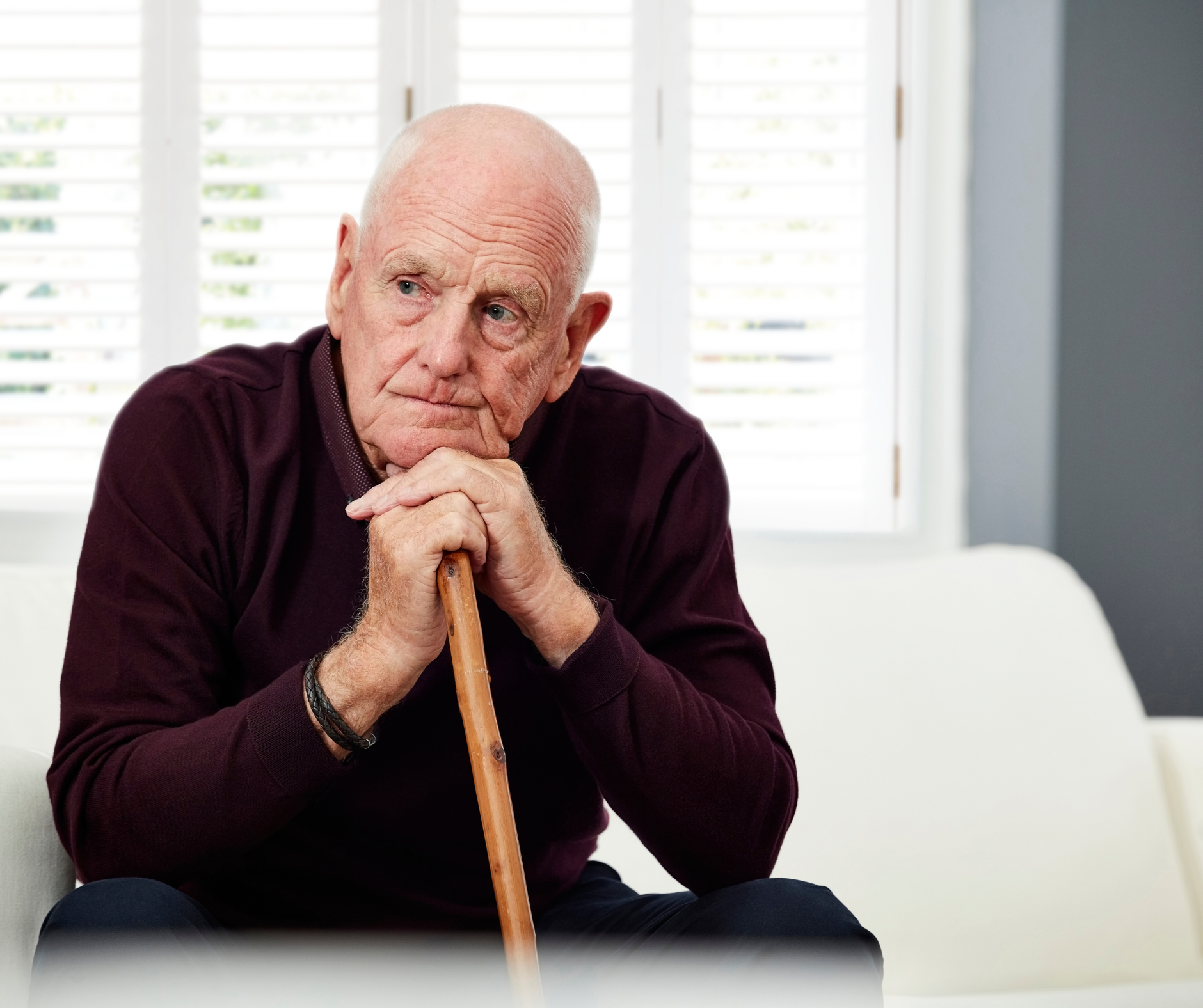 Older man sitting alone at home with a cane representing senior living alone and social isolation
